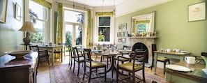 Classic dining room with a large table, comfortable chairs, and a fireplace, surrounded by artwork and a large window.