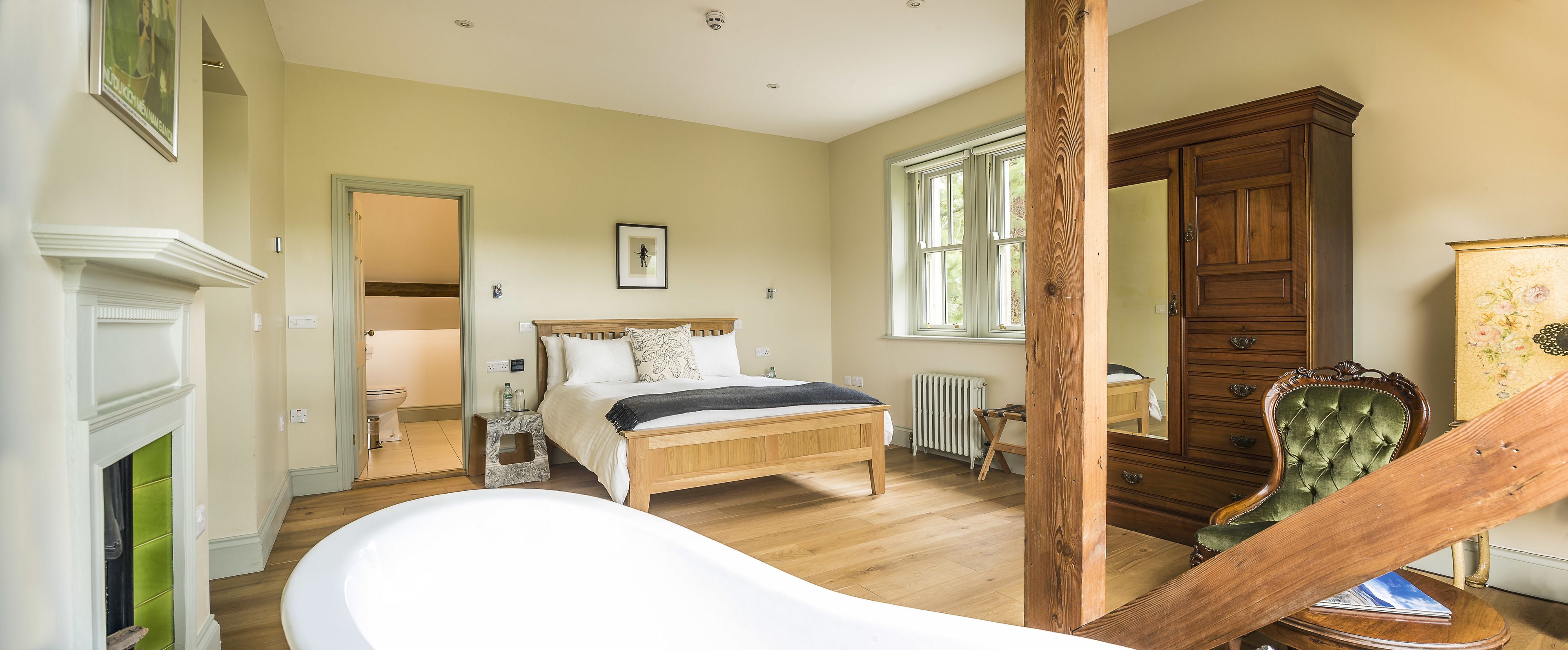 Een slaapkamer met een houten bed, een witte badkuip, een houten dressoir en een spiegel.