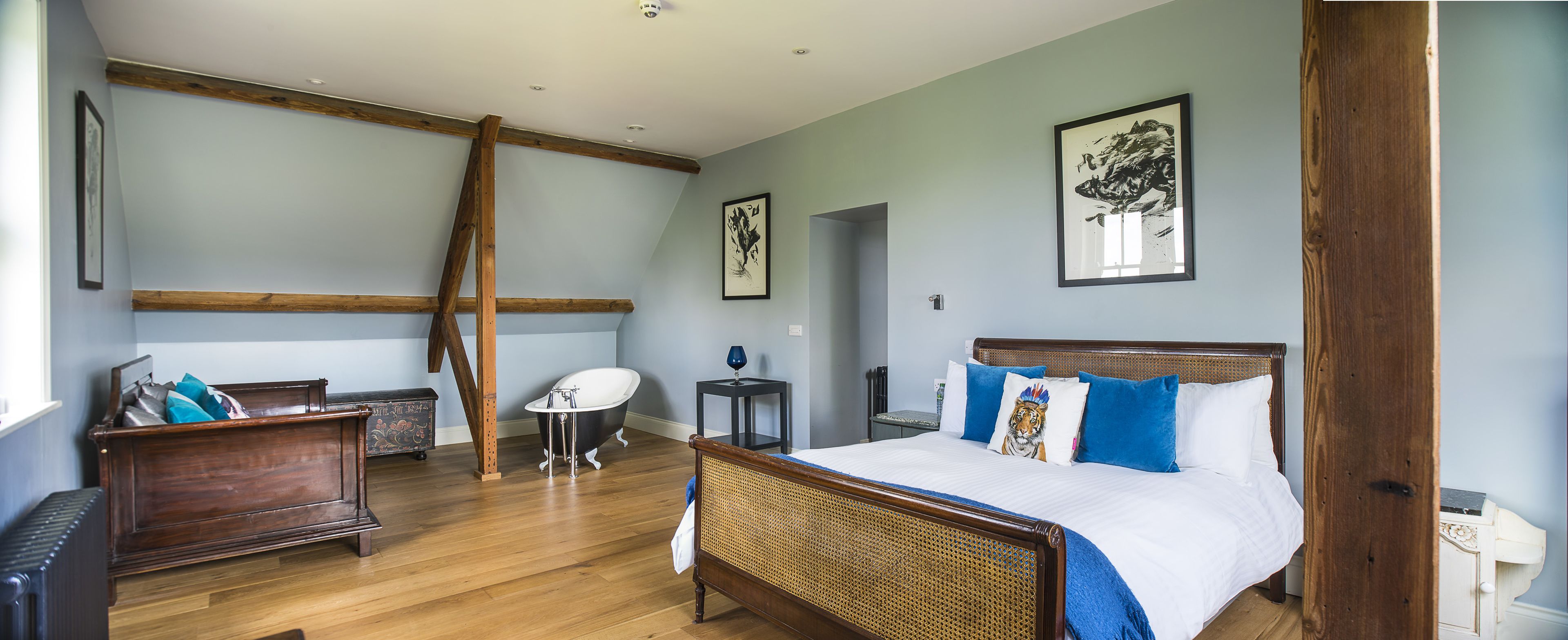 A spacious bedroom with a large bed, a wooden dresser, a clawfoot bathtub, and a small table with a lamp.