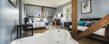 Un dormitorio con una bañera grande, una cama con cabecera de madera y una ventana con vistas a árboles.