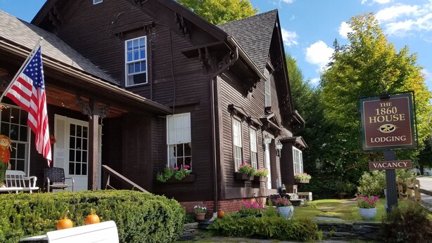 A wooden house with a porch, an American flag, and a sign indicating it is a lodging with a vacancy. - 1860 House Inn and Vacation Rental Home (Stowe)