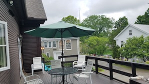 A wooden deck with outdoor furniture, including chairs and a table, under a green umbrella. - 1860 House Inn and Vacation Rental Home (Stowe)