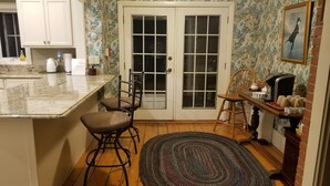 A kitchen with a marble countertop, two bar stools, a wooden dining table with chairs, a patterned rug, and a framed picture on the wall. - 1860 House Inn and Vacation Rental Home (Stowe)