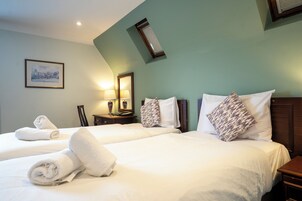 A hotel room with two beds, white linens, and towels. There is a framed picture on the wall and a small table with a lamp.