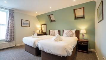 A hotel room with two beds, a window with curtains, a radiator, and a nightstand with a lamp.