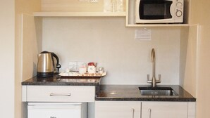 Una cocina compacta con un refrigerador blanco, un microondas, un lavabo y una pequeña encimera con una tetera y algunos objetos.