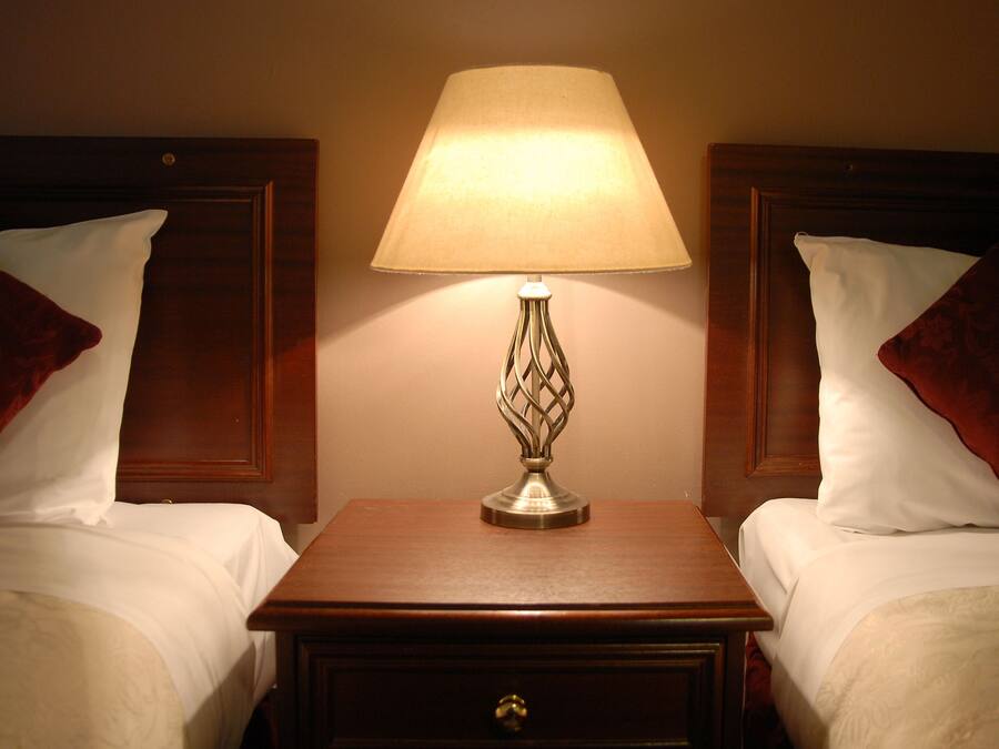 Une chambre d’hôtel avec deux lits, chacun doté d’une tête de lit en bois, d’une table de chevet avec une lampe et d’oreillers rouges.