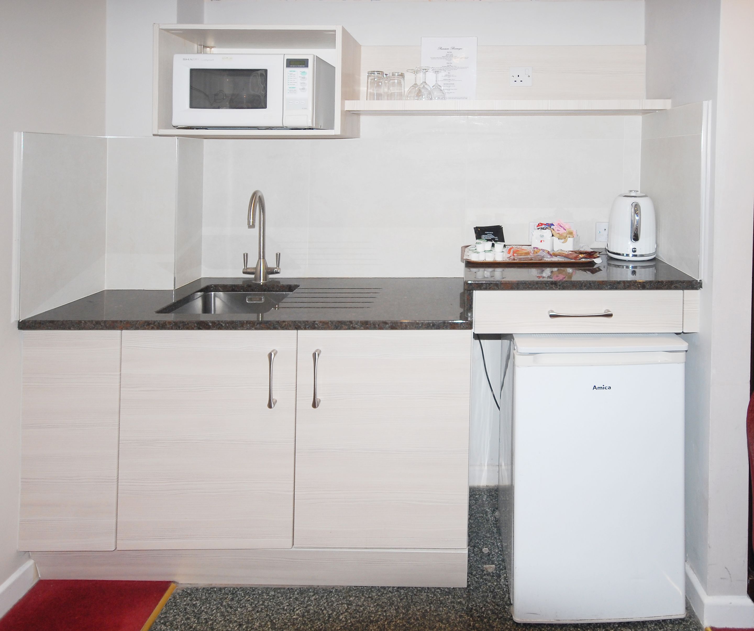 A compact kitchen with a microwave, sink, and a small refrigerator.
