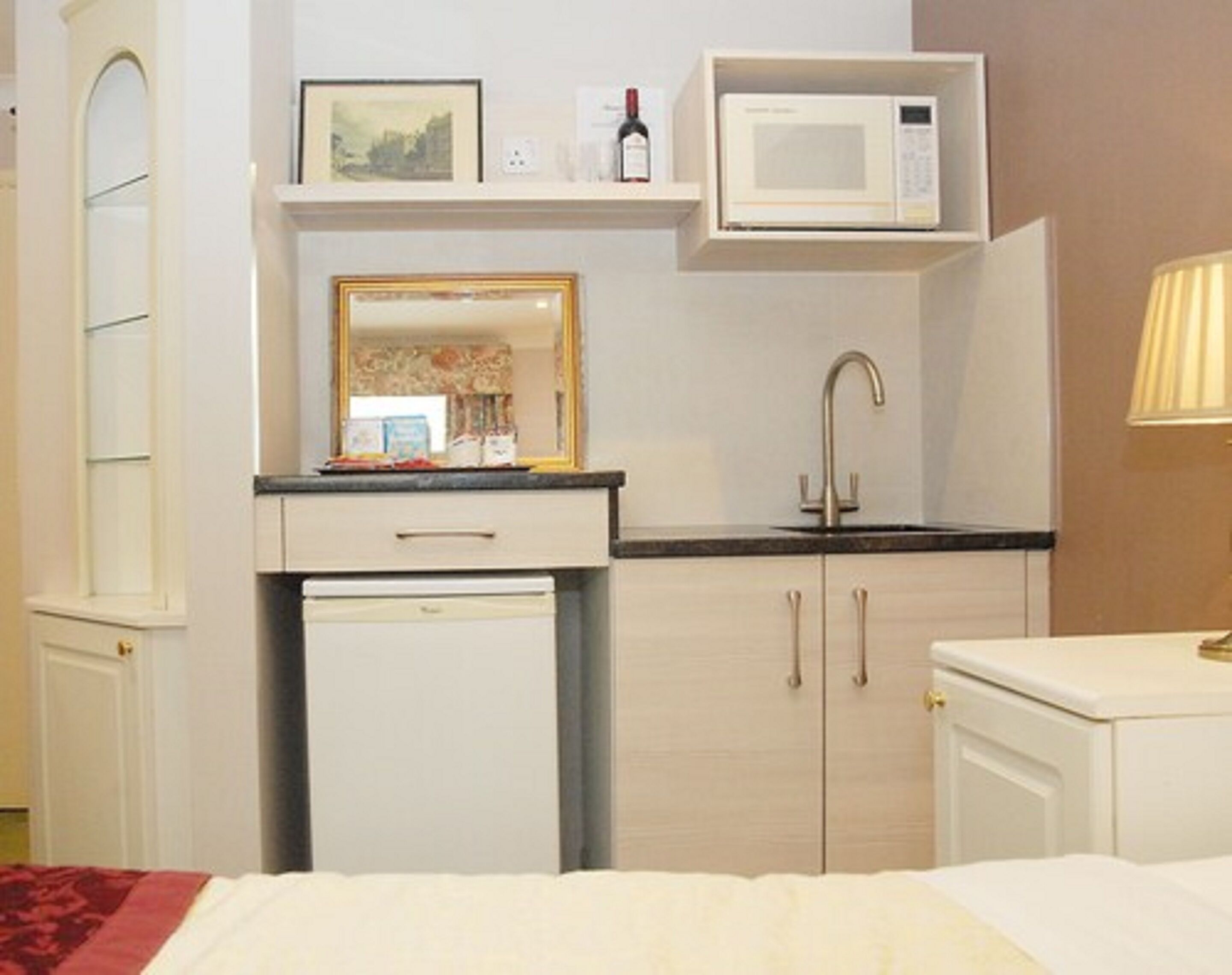 Ein kleines Hotelzimmer mit einem Bett, einer kompakten Küchenzeile inklusive Mikrowelle, Spüle und kleinem Kühlschrank.