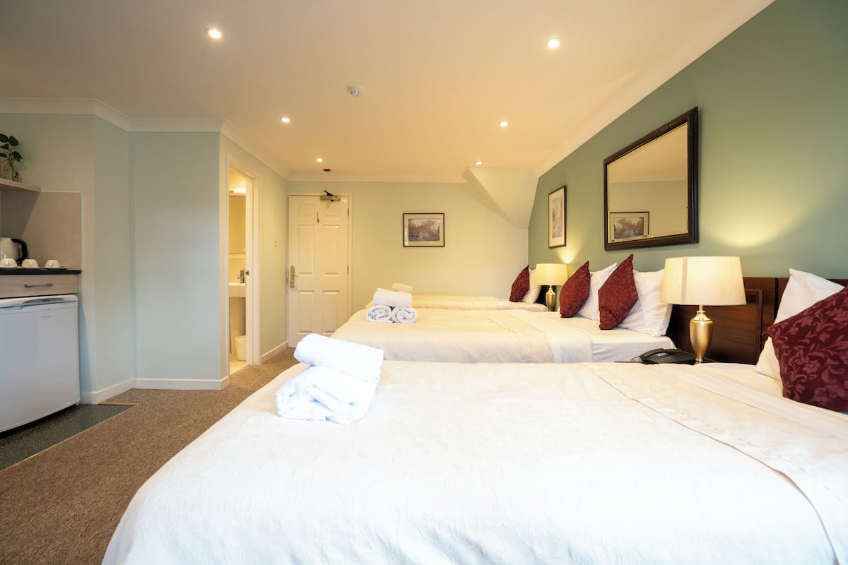 A hotel room with two beds, a desk with a kettle, and a mirror on the wall.