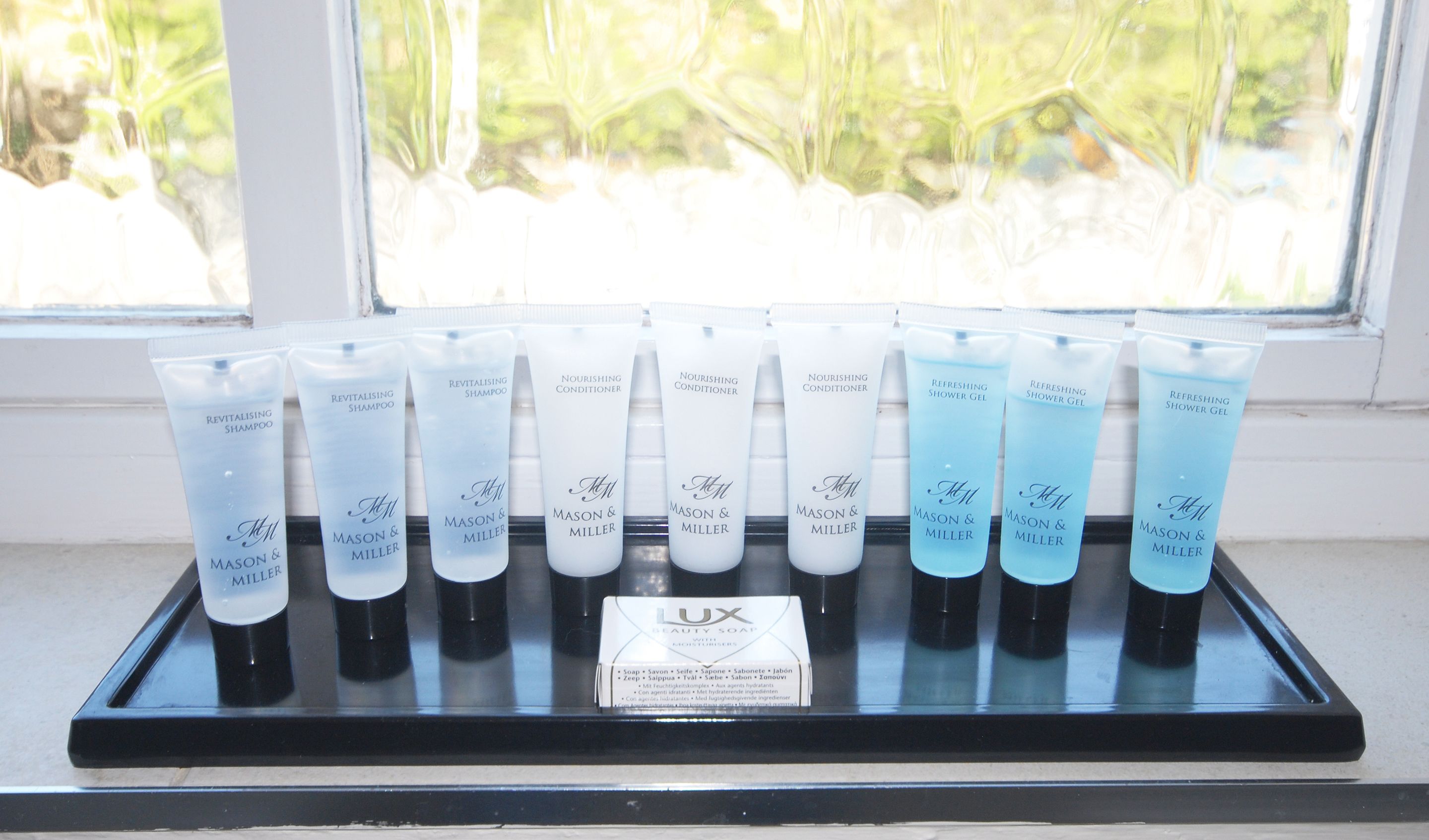 A display of beauty products on a black tray by a window.