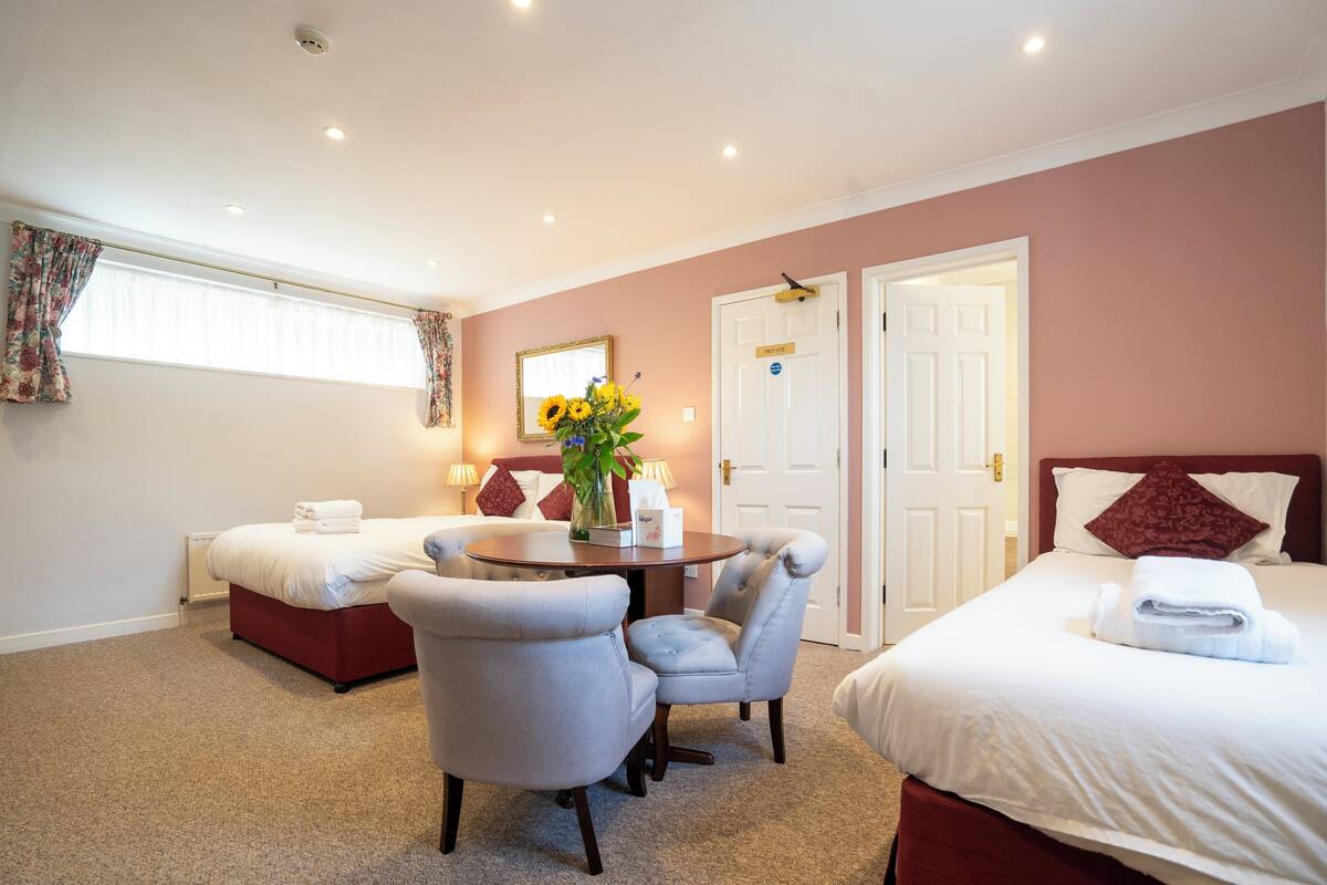 A hotel room with a bed, two armchairs, a small table with a vase of flowers, and a window with curtains.