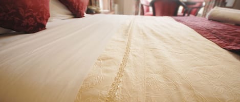 A bed with a white and beige bedspread, red pillows, and a chair in the background.