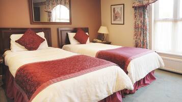 A hotel room with two beds, each with a red bedspread and white pillows. There is a nightstand with a lamp and a telephone, a mirror on the wall, and a framed picture above the bed.