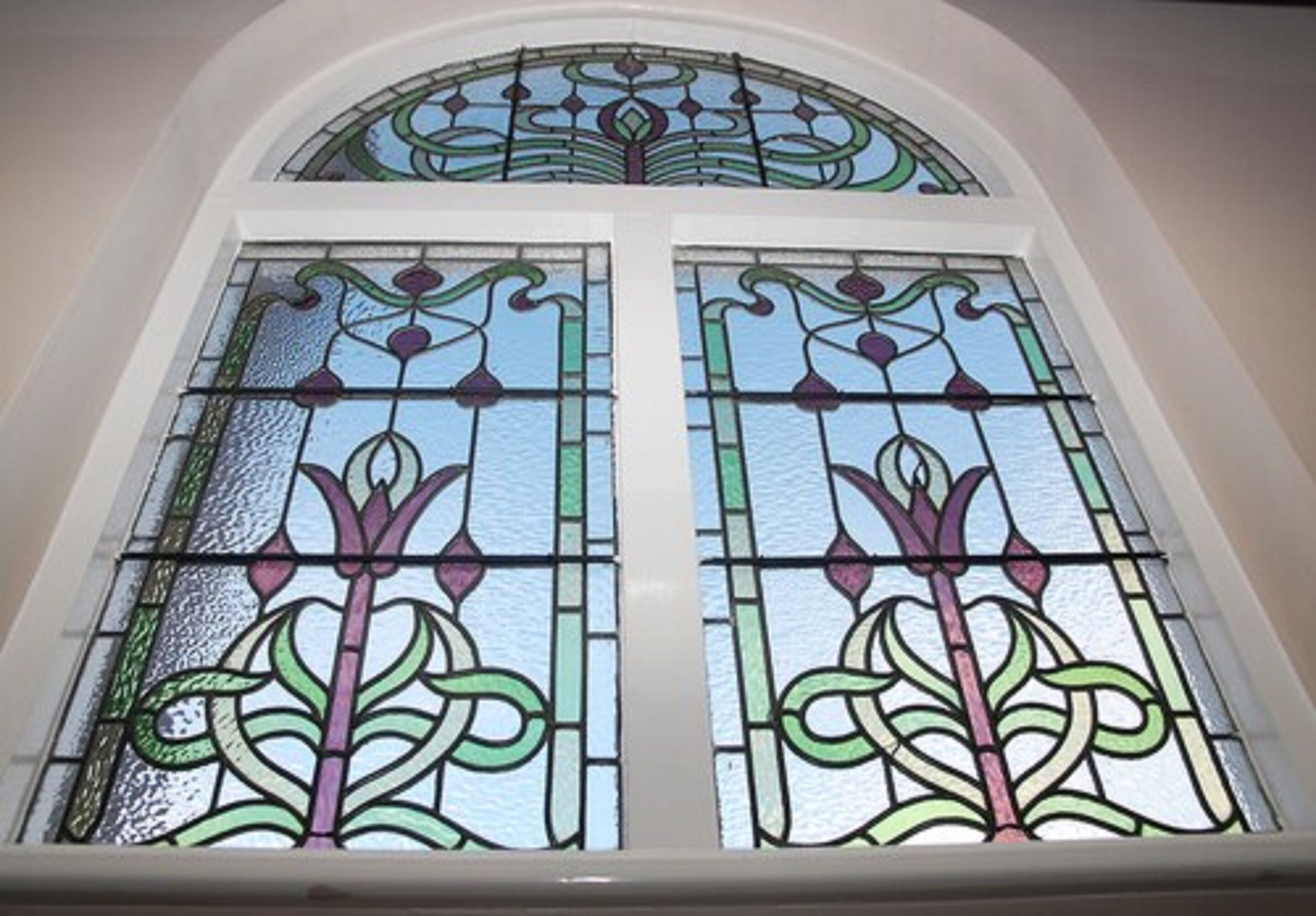 Une fenêtre en vitrail ornée de motifs floraux complexes et surmontée d’une arche semi-circulaire.