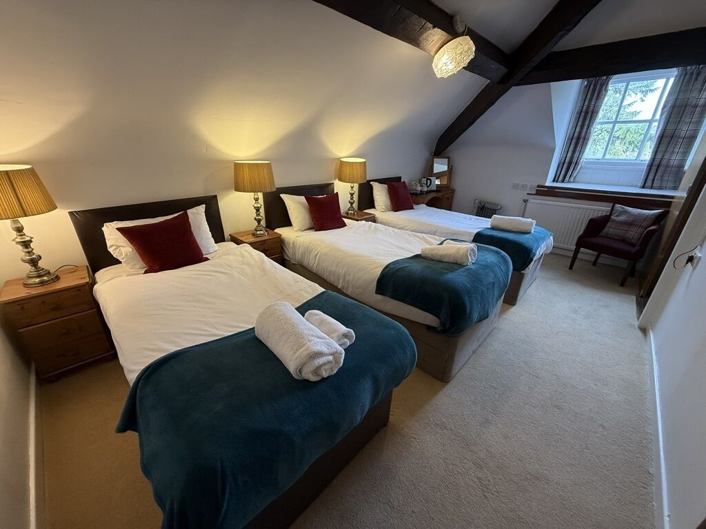 A hotel room with two beds, each with a white comforter and teal bedspread, and a small wooden chair.