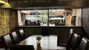 A restaurant with a bar area, a wooden table, and black leather chairs. - Royal Goat Hotel (Caernarfon)