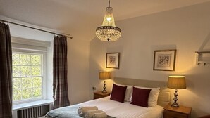 A neatly made bed with a grey blanket and two towels, two bedside lamps, a chandelier, and two framed pictures on the wall. - Royal Goat Hotel (Caernarfon)