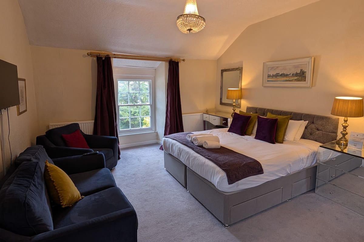A bedroom with a large bed, a sofa, a desk, and a window with curtains.
