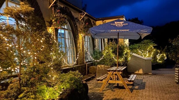 An outdoor patio area with a table and chairs, a hanging umbrella, and a stone wall. - Royal Goat Hotel (Caernarfon)