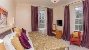 A hotel room with a bed, a desk, a chair, and a TV.