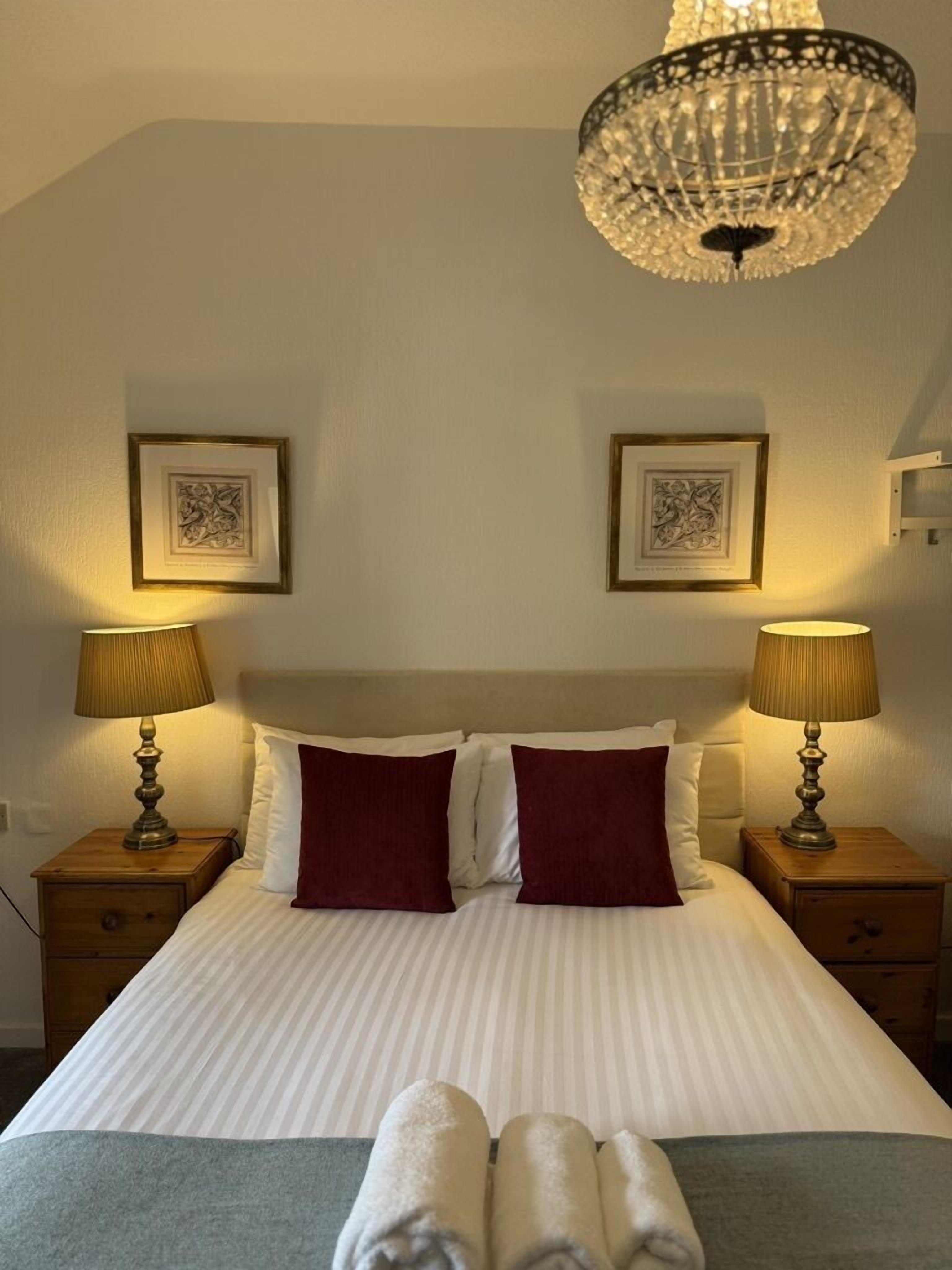 A neatly made bed with two pillows, two bedside lamps, and a chandelier.
