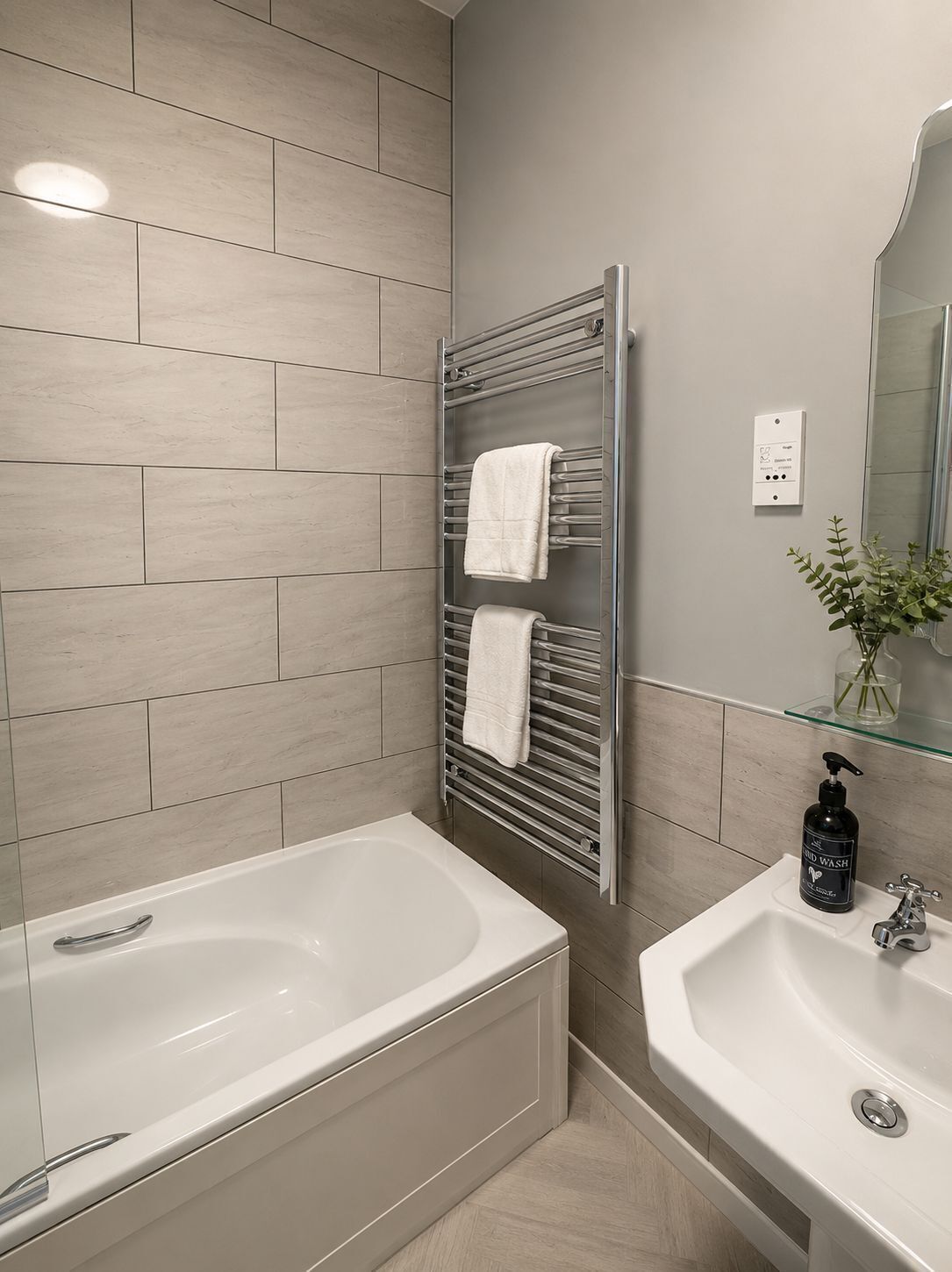 A modern bathroom with a bathtub, a glass shower enclosure, a towel rack with two towels, a sink, and a mirror.
