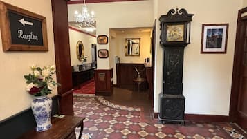 A reception area with a red and beige patterned carpet, a reception desk, a vase with flowers, a clock, and framed pictures on the wall.