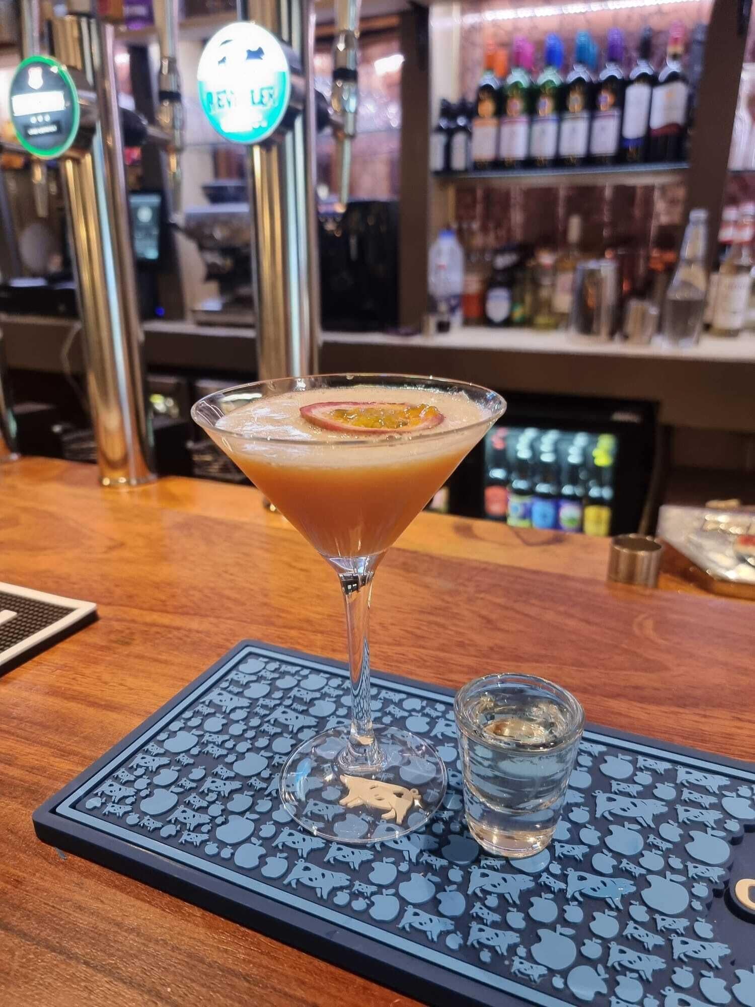 A martini glass with a cocktail on a bar counter, a shot glass, and a coaster with animal designs.