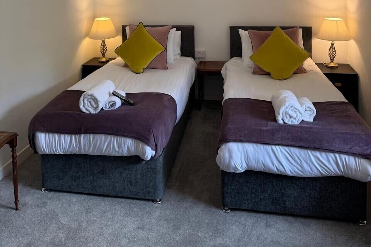 A hotel room with two beds, each with a pillow, a bedside table with a lamp, and a framed picture on the wall.
