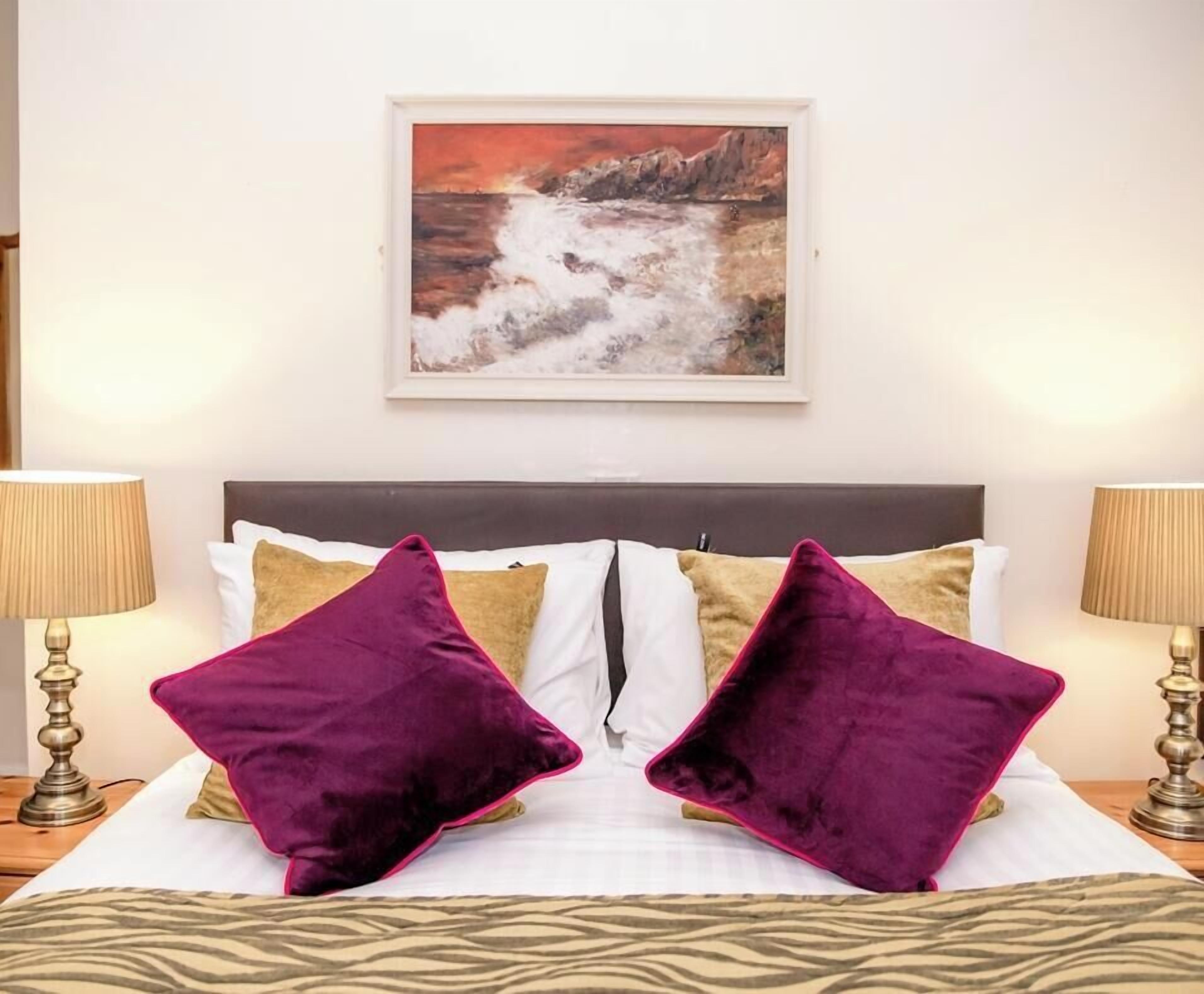A hotel room with a bed, two lamps, a painting, and a zebra-patterned bedspread.