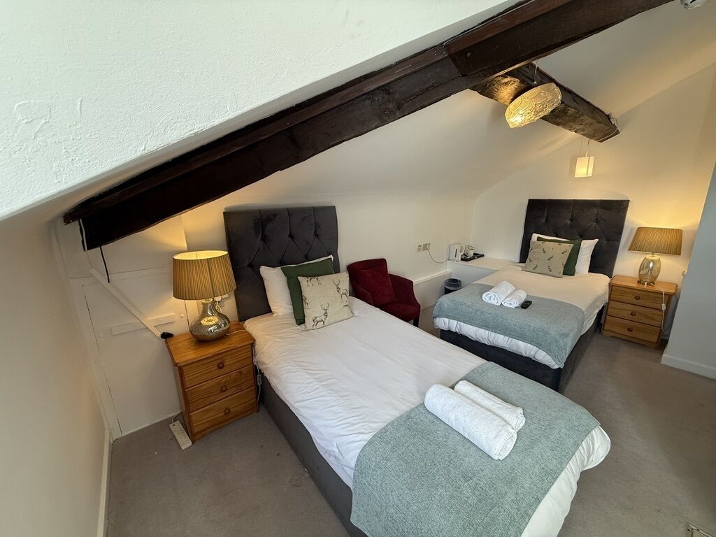 A bedroom with two beds, a red chair, bedside tables with lamps, and a sloped ceiling.