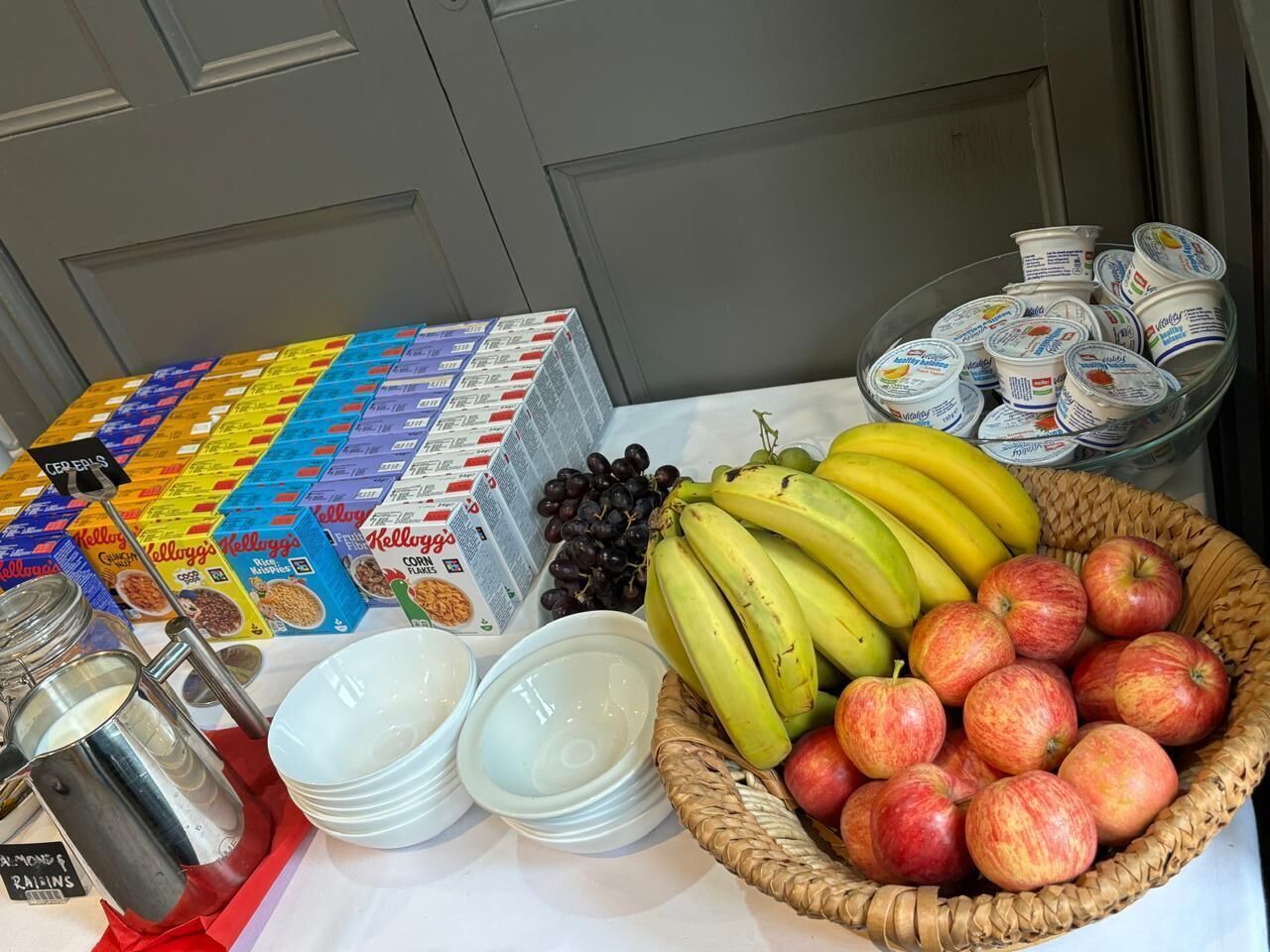 A table with various food items including cereal boxes, bananas, apples, and yogurt containers.