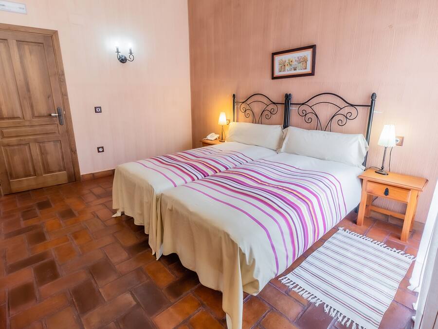 Un dormitorio con una cama, dos mesitas de noche, una puerta de madera y una lámpara fijada a la pared.