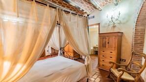 A bedroom with a four-poster bed, wooden wardrobe, and a rocking chair. - Hotel Rural La Sinforosa (Alange)
