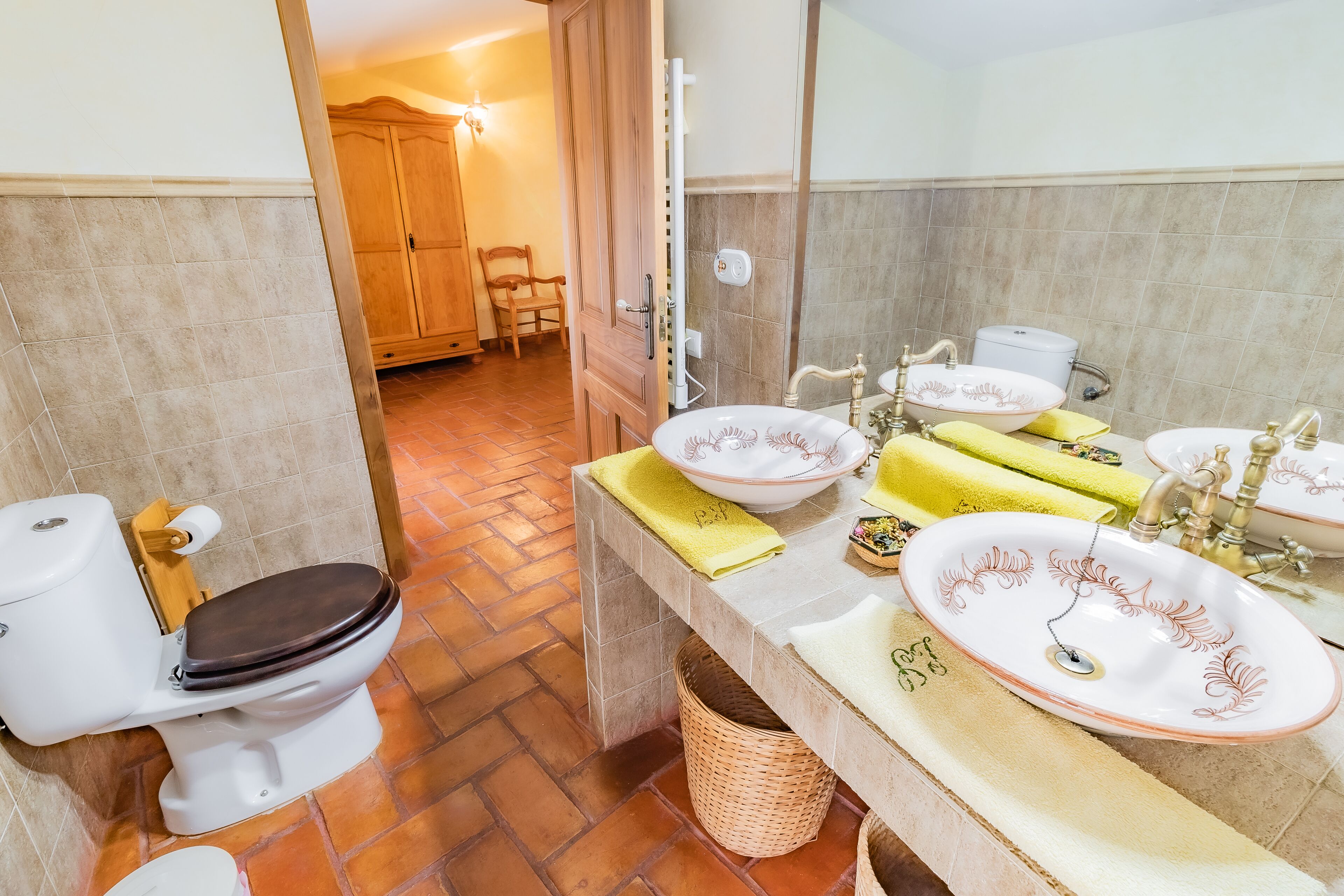 A bathroom with a toilet, two sinks with decorative bowls, a mirror, and a wooden cabinet.