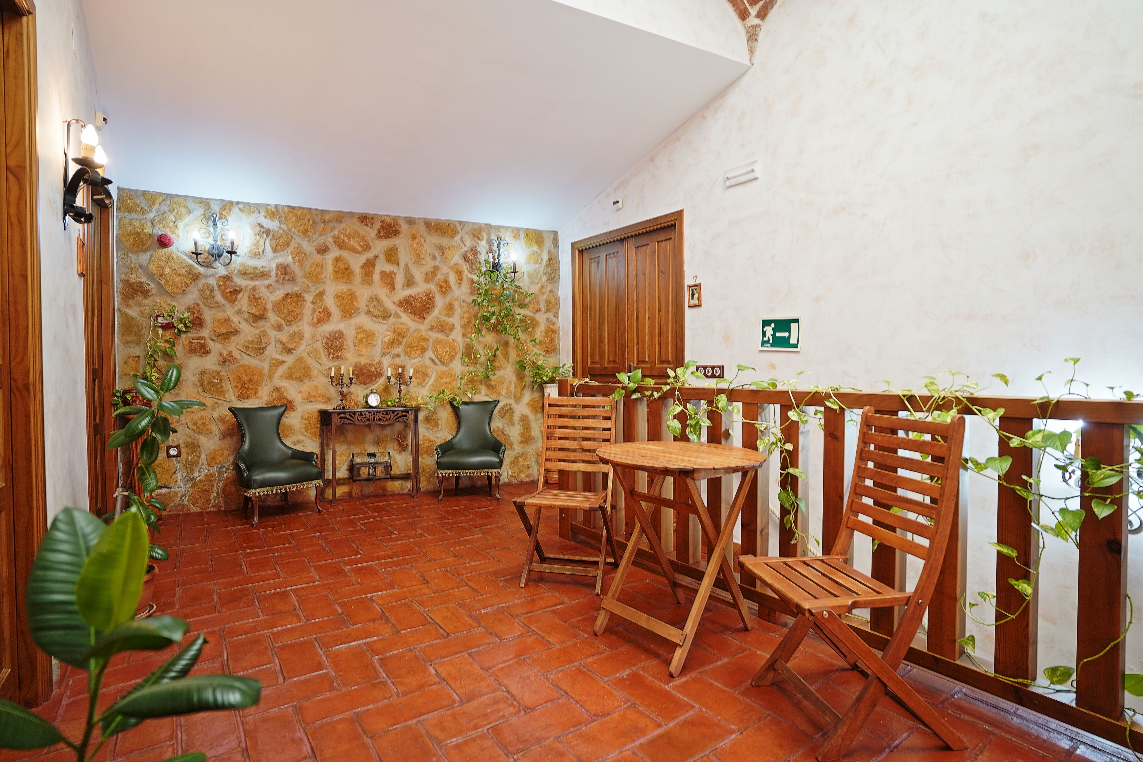 A patio area with a stone wall, wooden furniture, and potted plants.