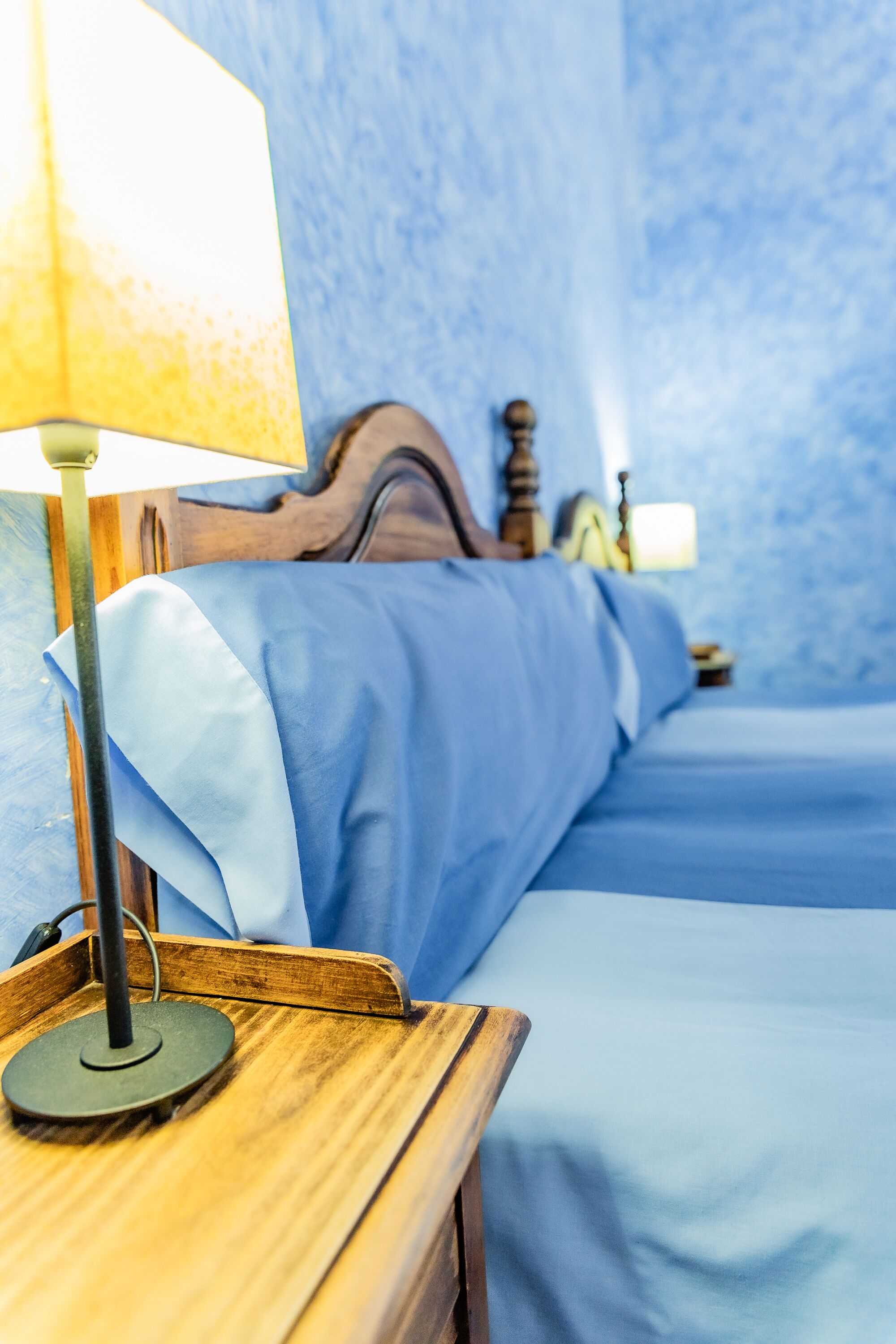 Une chambre d’hôtel avec une table de chevet en bois, une lampe et un lit avec une literie bleue.