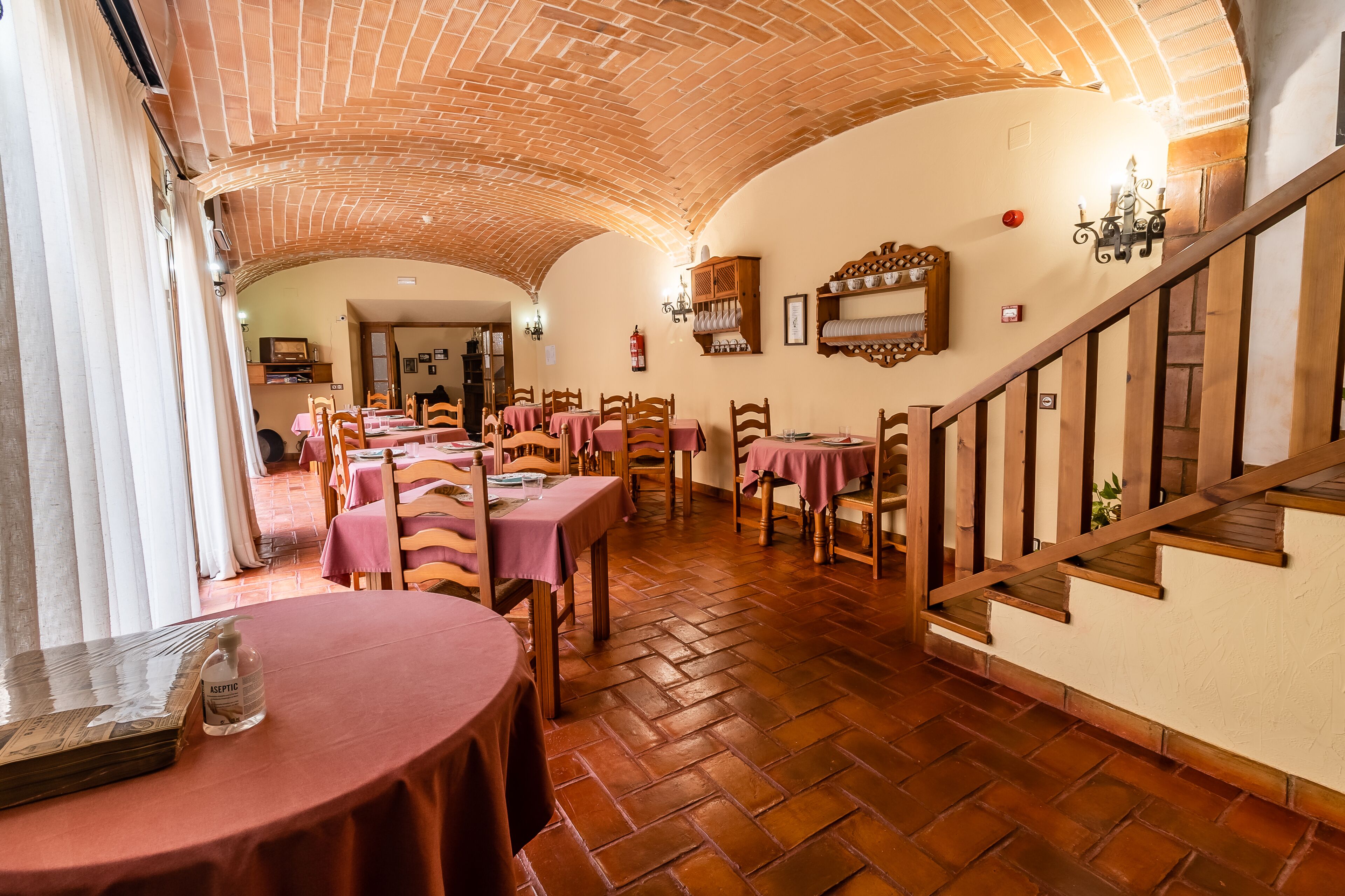 Un restaurante con suelo de ladrillo, mesas y sillas de madera. Se observa una escalera a la derecha.