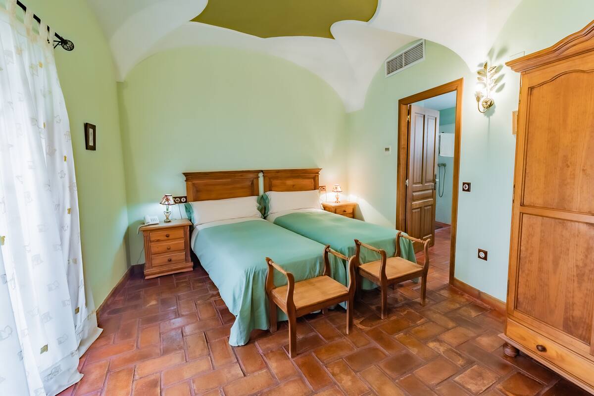 A bedroom with two beds, wooden furniture, and a tiled floor.