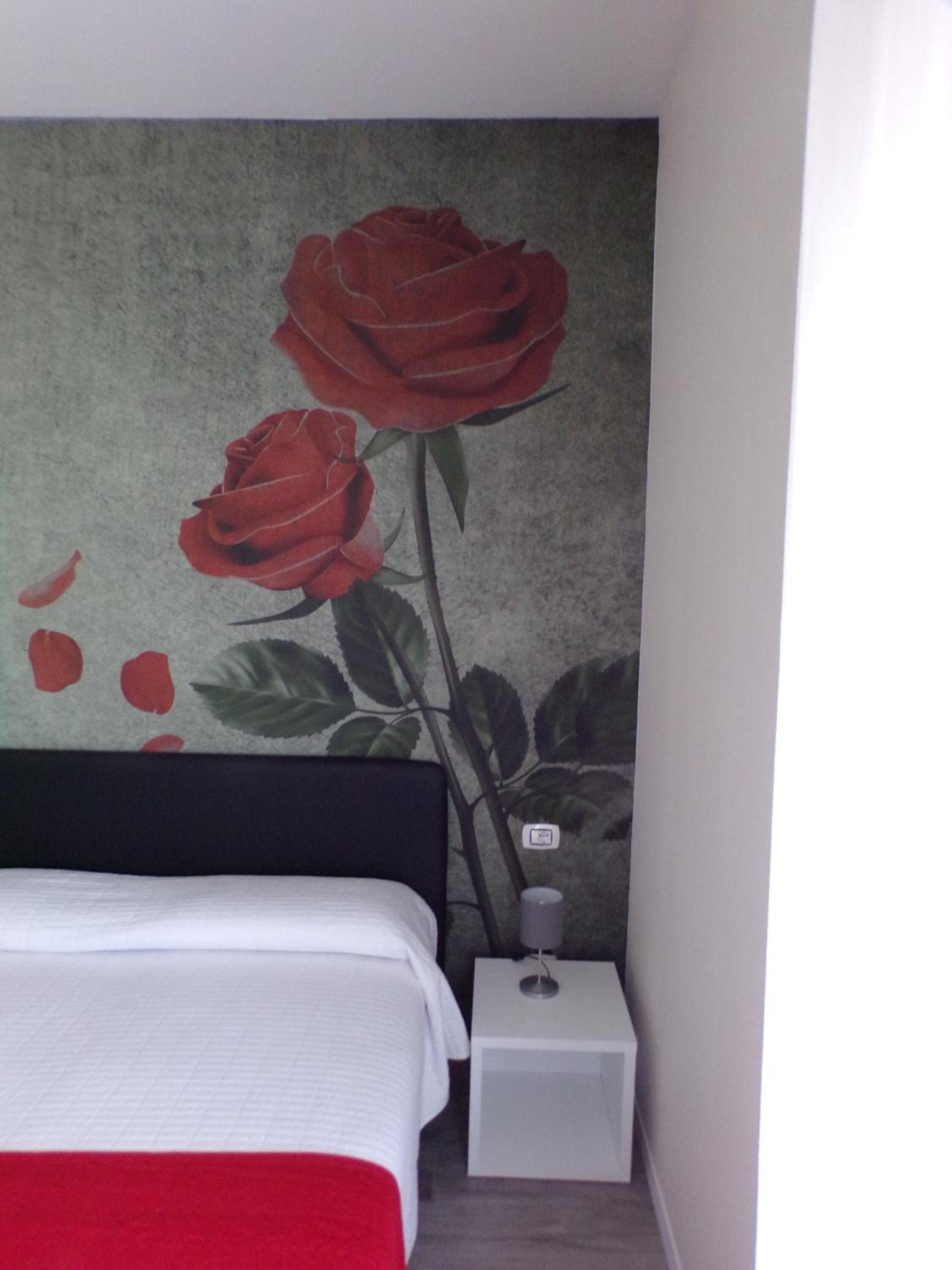 A bedroom with a bed, a nightstand, and a wall with a rose mural.