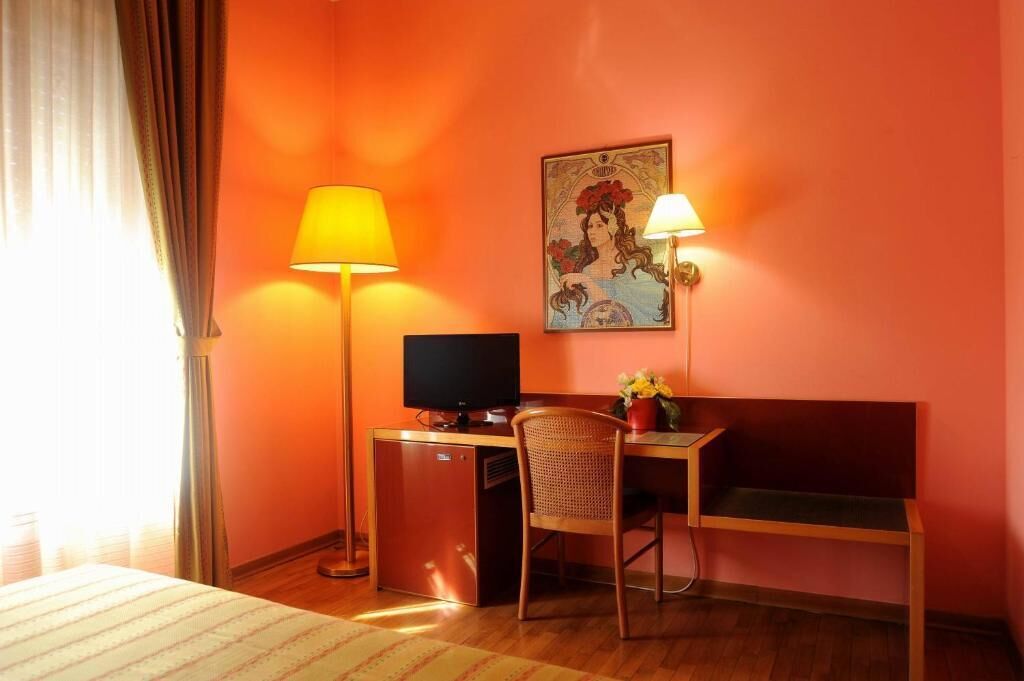 A hotel room with a desk, a chair, a television, and a painting on the wall.