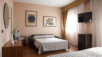 A hotel room with a bed, a desk with a chair, a television, and two framed artworks on the wall.