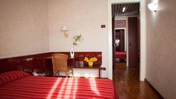 Una camera d'albergo con un letto, una scrivania, una sedia, una lampada e un vaso con fiori.