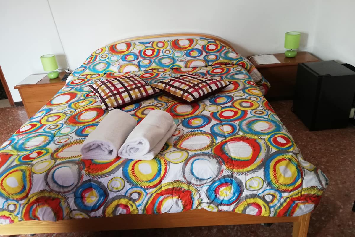 Un lit recouvert d’une courtepointe aux motifs circulaires et colorés, avec deux oreillers et deux serviettes enroulées.