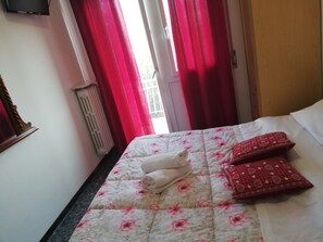 Una cama bien tendida con un edredón floral, dos almohadas y una toalla enrollada.