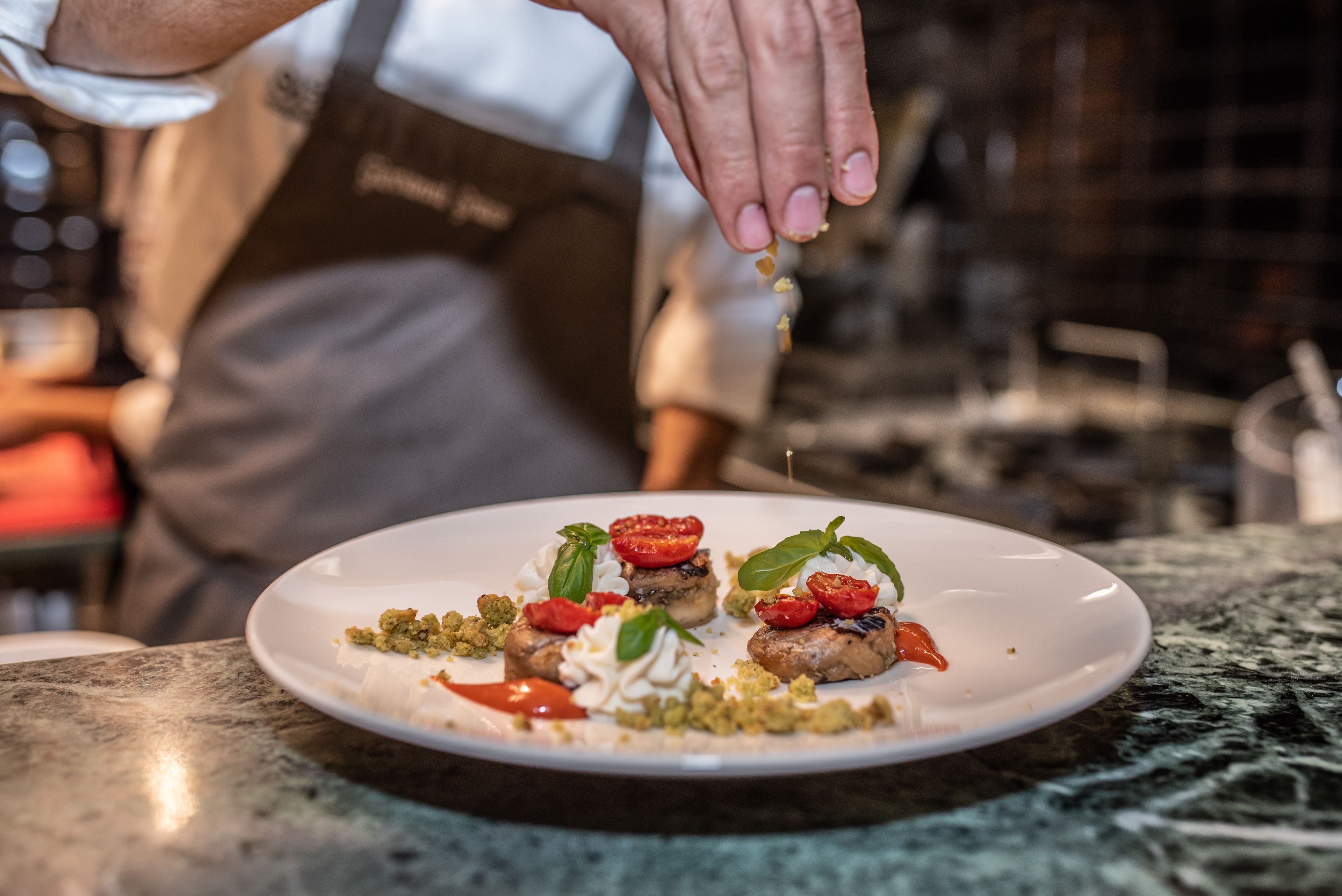 Un chef prépare un plat sur une assiette blanche posée sur un plan de travail en marbre.