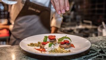 Un chef prépare un plat sur une assiette blanche posée sur un plan de travail en marbre.