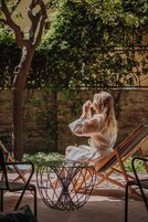 A person sitting on a wooden lounge chair in a garden area with a brick wall and greenery in the background.