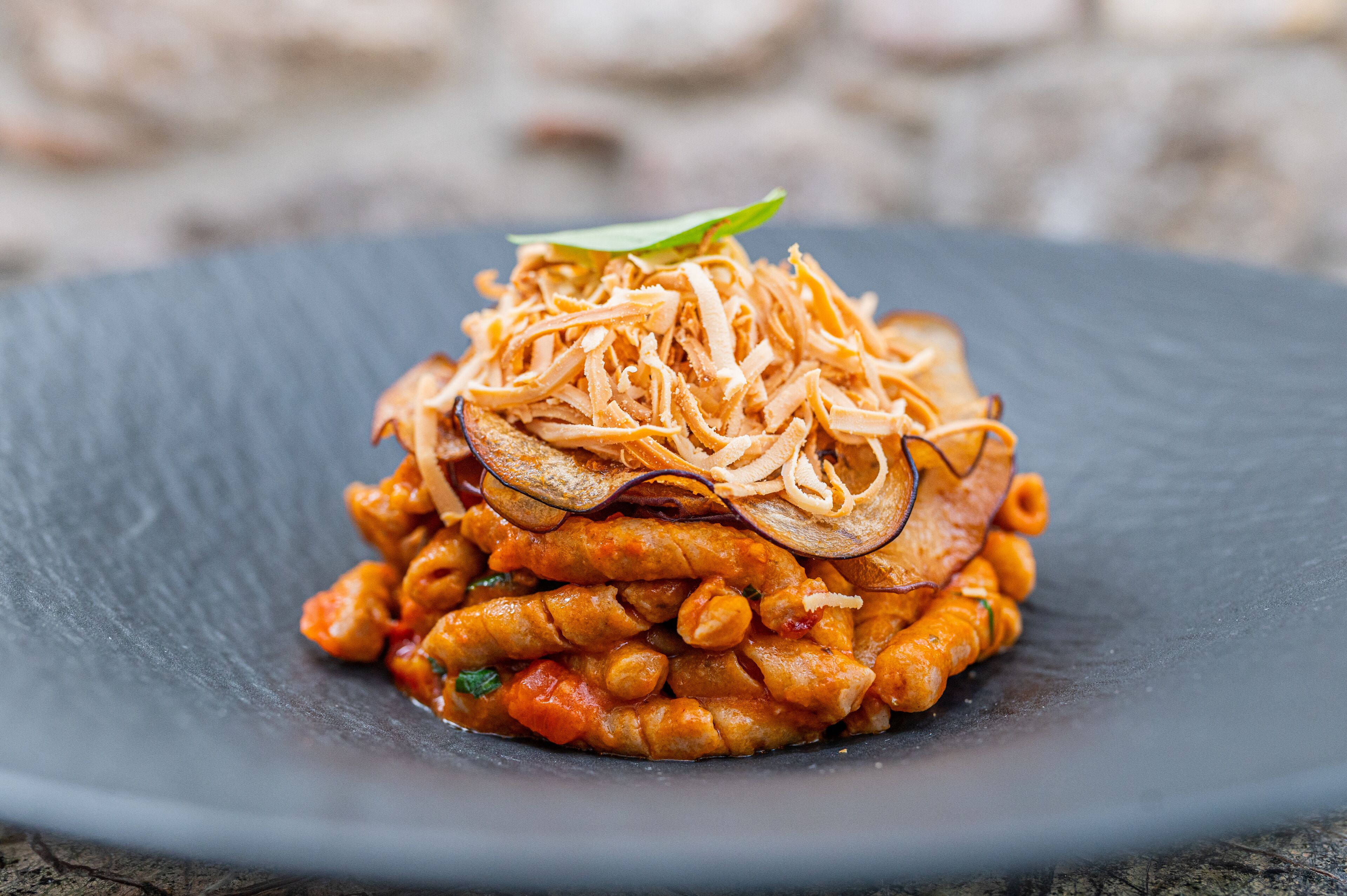 A plate of pasta with a garnish on a dark plate.